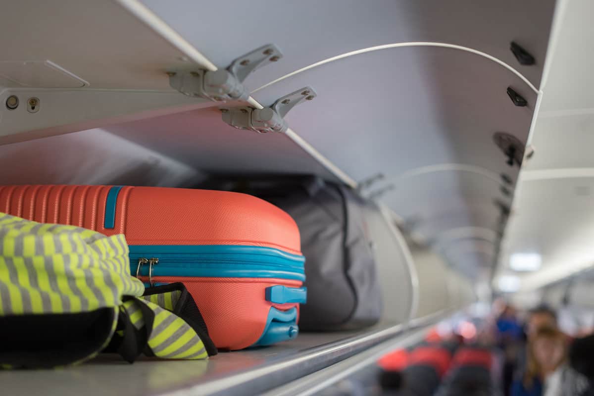 Carry-on luggage on the top shelf over head on airplane, passenger put bag cabin compartment
