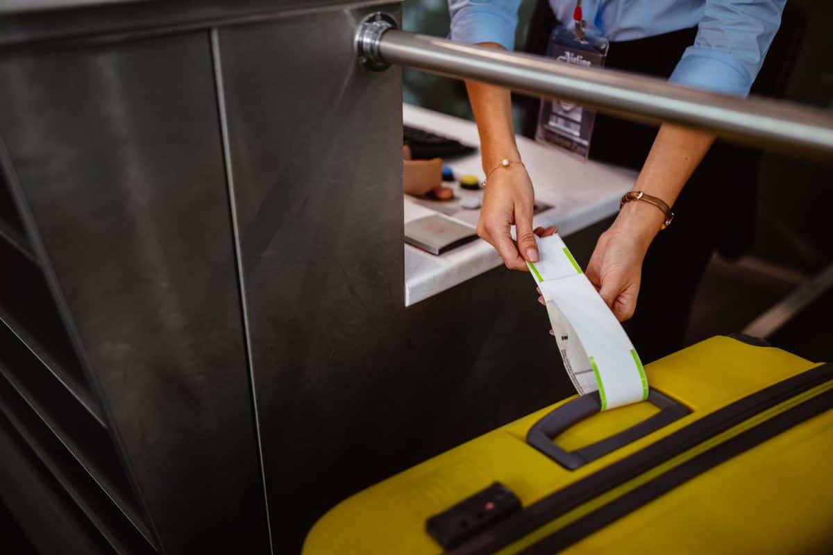 Close-up of airport attendant attaching label on suitcase at airline check-in desk

