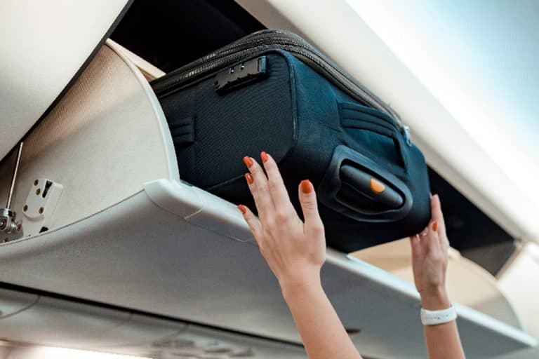 Flight attendant placing travel bag in overhead baggage locker, What Is The Weight Limit For A Carry On Bag For United Airlines?