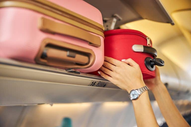 Hands laying down a carry-on baggage on an upper shelf - Are Carry-On Bags Weighed [Do Airlines Actually Weigh Them]