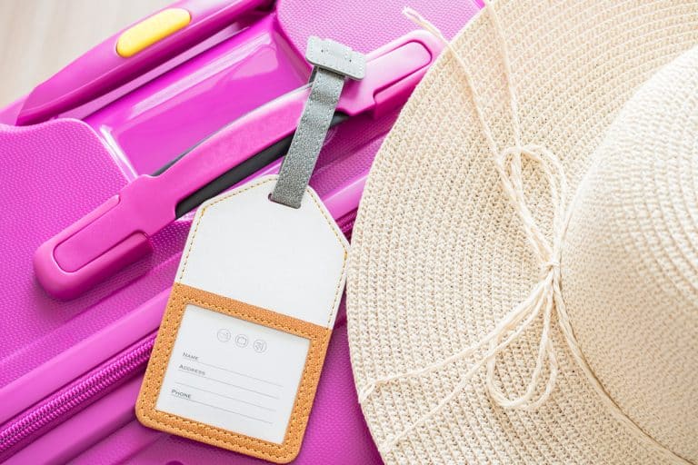 Luggage tag and white hat on pink suitcase, Do Carry-On Bags Need Tags