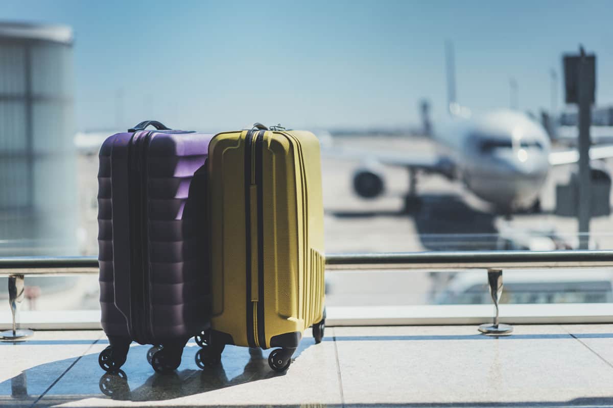 Suitcases in airport departure lounge, airplane in background, summer vacation concept, traveler suitcases in airport terminal waiting
