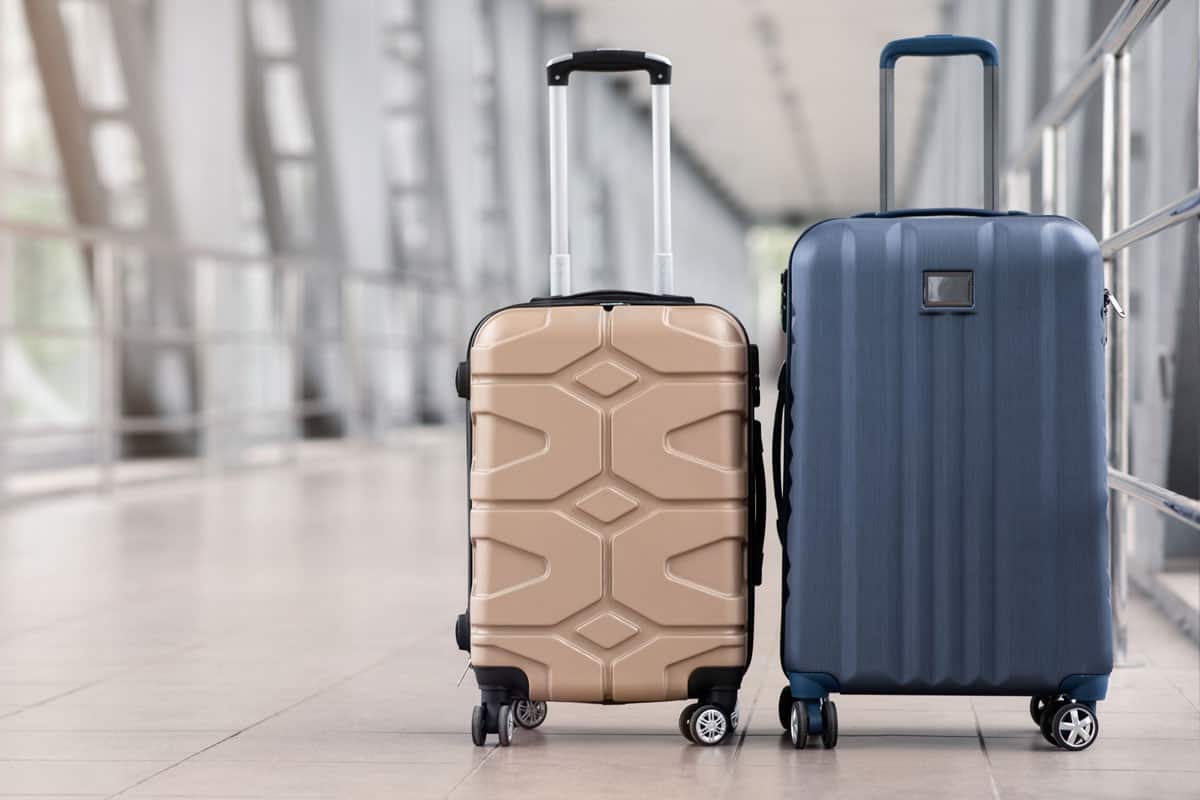 Two stylish suitcases standing in empty airport hall, unrecognizable traveller's luggage waiting in terminal, creative banner
