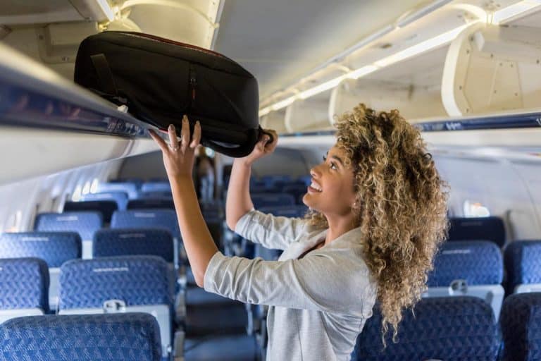 A young woman places luggage in airline overhead bin, Should I Put My Make-up In My Carry-On?