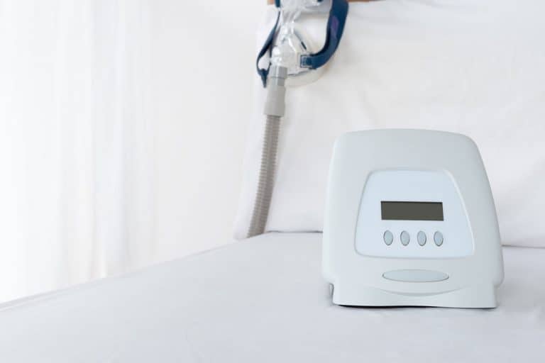bright photo of a cpap machine on a white room, white wall, white bed sheet, Do CPAP Machines Count As Carry On Luggage?