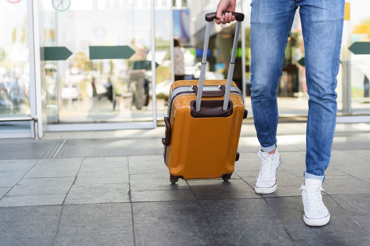 bright yellow carry on luggage on a clean environment, white shoes, blue jeans