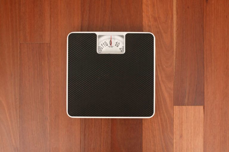 brown wood floor tile, black bathroom scale on the floor, Can I Use My Bathroom Scale To Weigh My Luggage? [And How To]