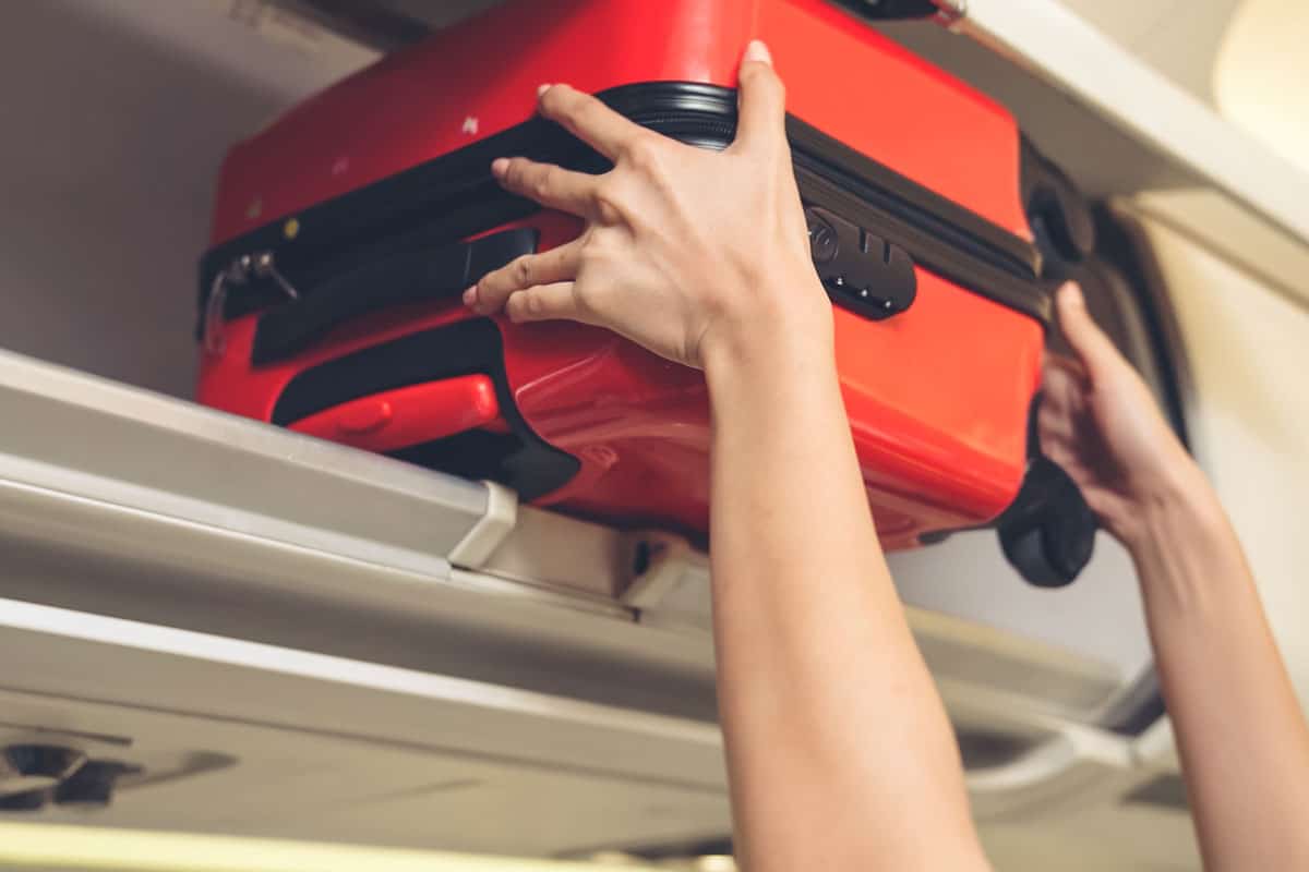 red carry on luggage on the plane overhead cabin, woman hands