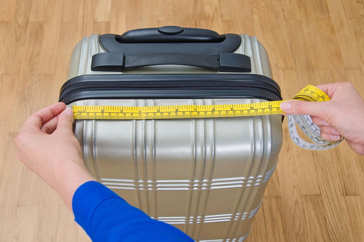 silver carry on luggage, measuring tape, woman hands, blue clothing