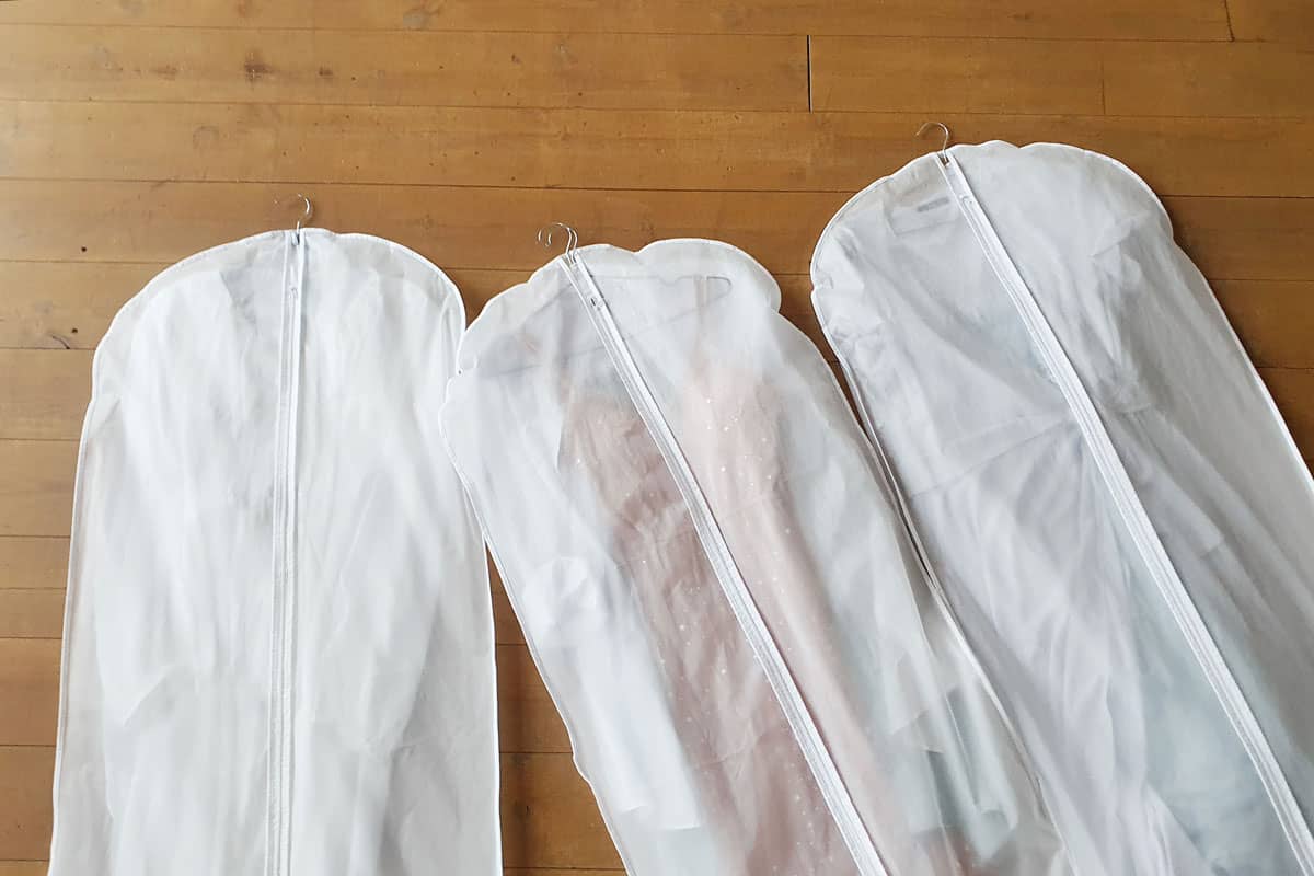 three white garment bag, white long zipper, brown wood floor tile,