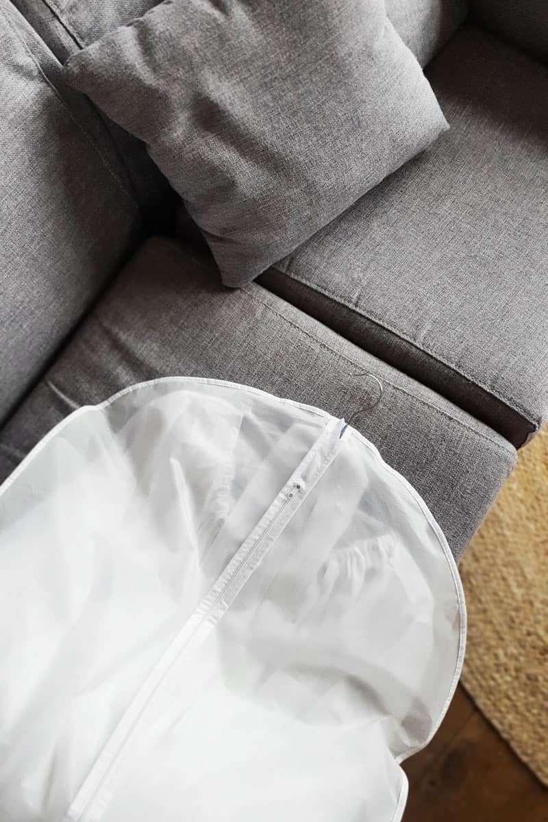 white garment bag, brown wood floor tile, grey sofa, grey pillow