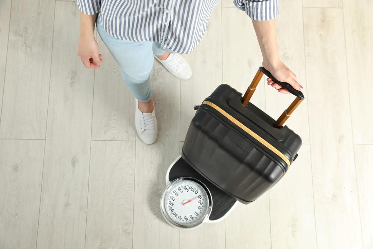 Woman weighing a black carry on luggage, white shoes, light colored jeans stripes