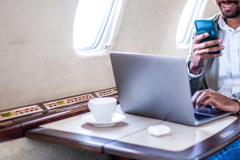 A businessman using laptop on a private jet, Can I Travel With A Laptop Battery? [Carry On Or Checked?]
