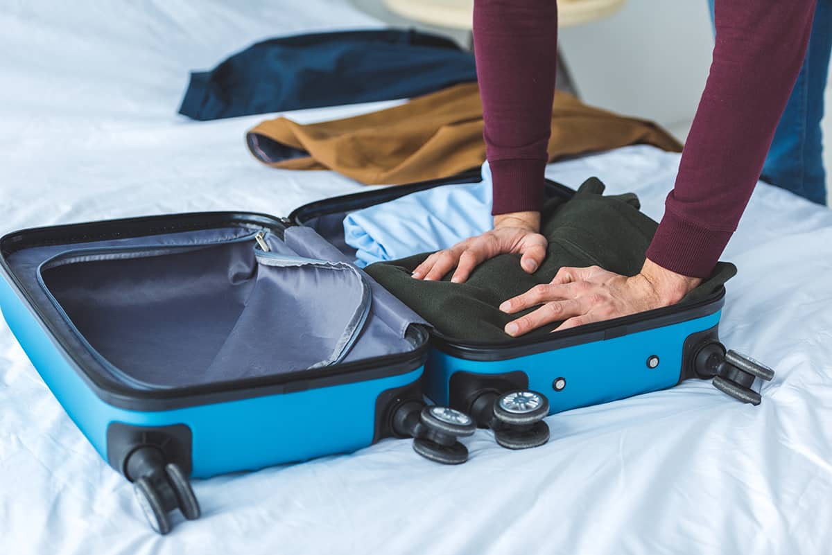 Cropped view of man packing clothes into travel bag