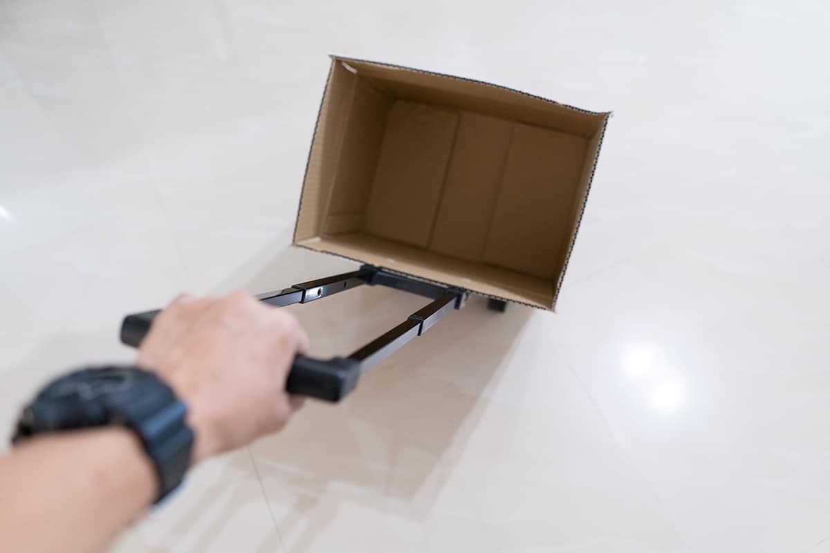 Hand holding a foldable trolley with empty brown box for shopping