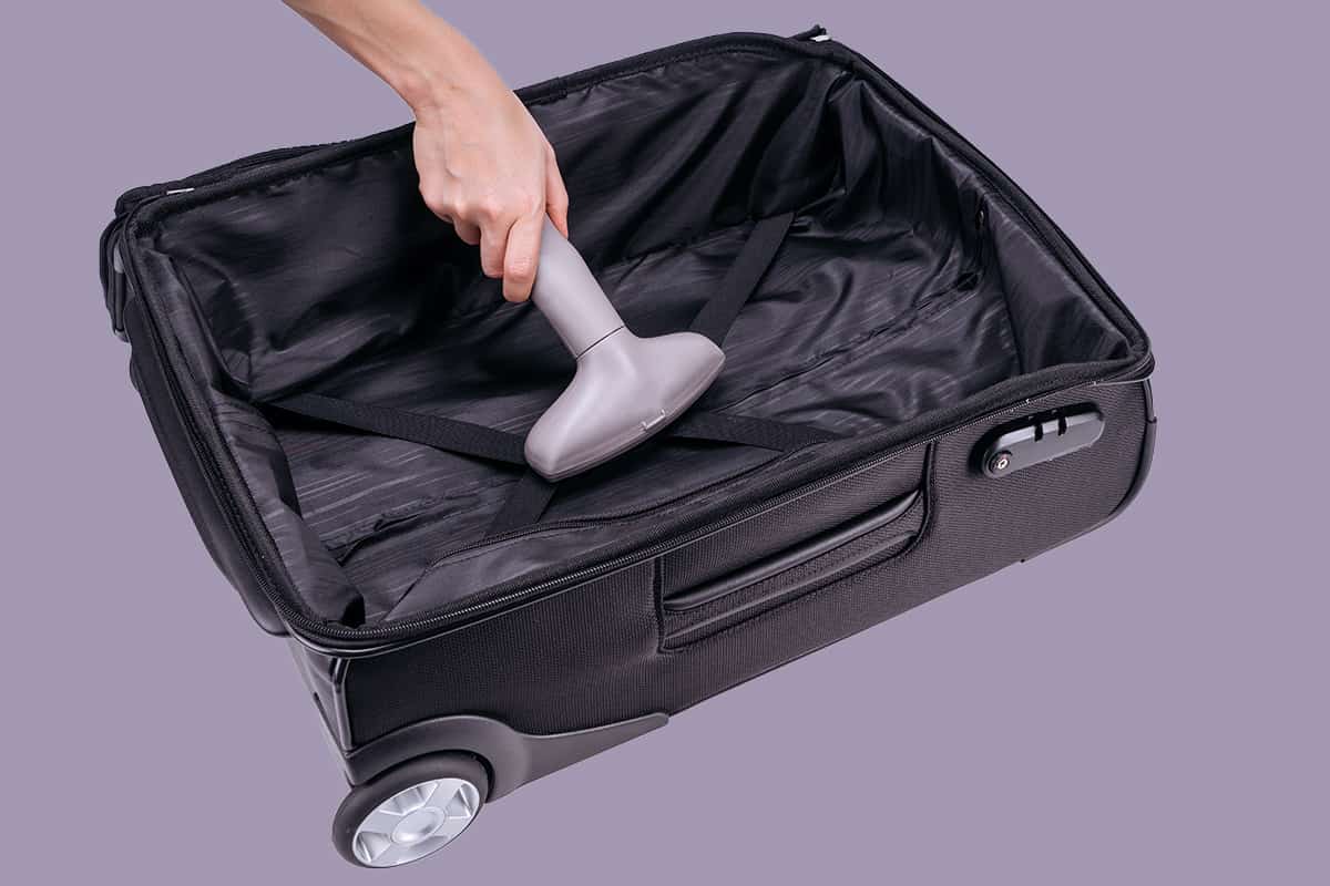 Hand vacuum-cleans black suitcase with the gray vacuum-cleaner