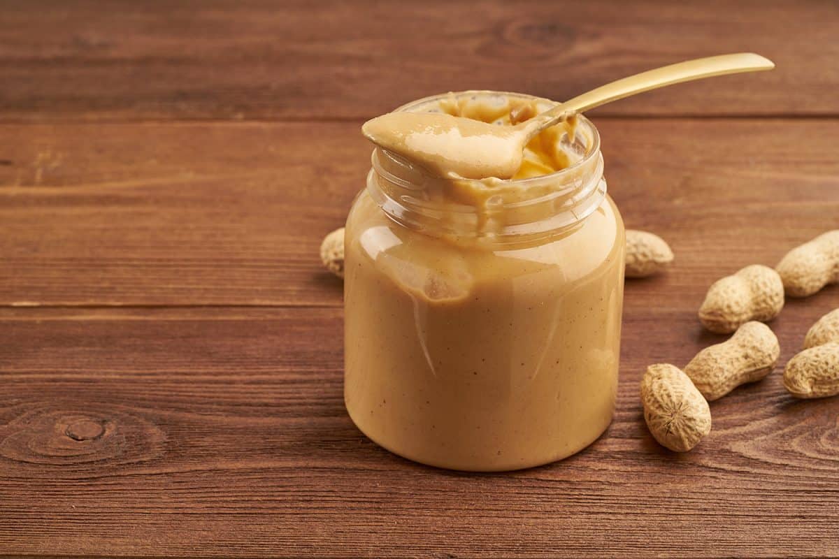 Jar of peanut butter and peanuts in a shell on brown wooden table