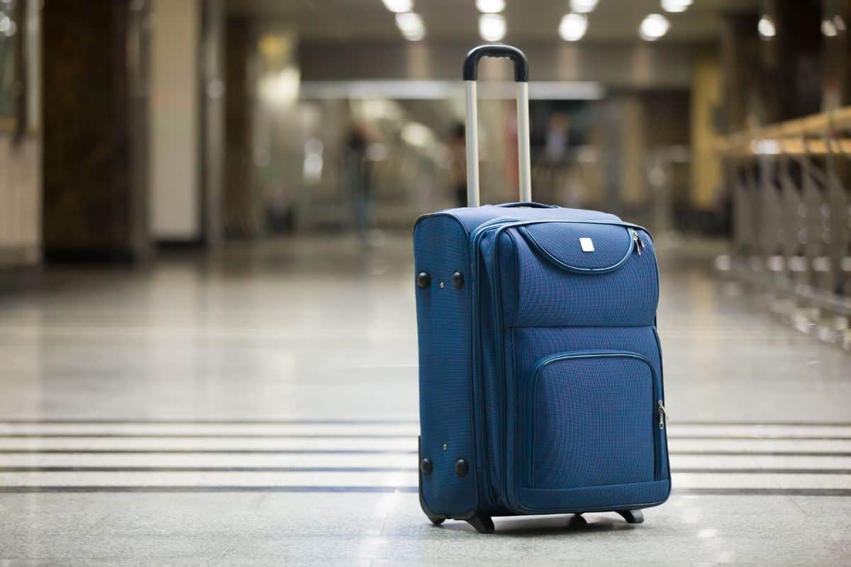 Large blue wheeled suitcase standing on the floor in modern airport terminal.