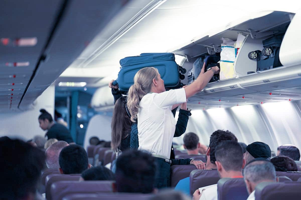 The stewardess helps the passengers to put their luggage in the cabin of the plane