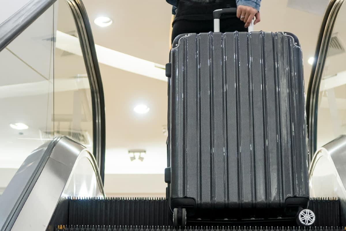 Traveler pulling modern hard luggage on escalator