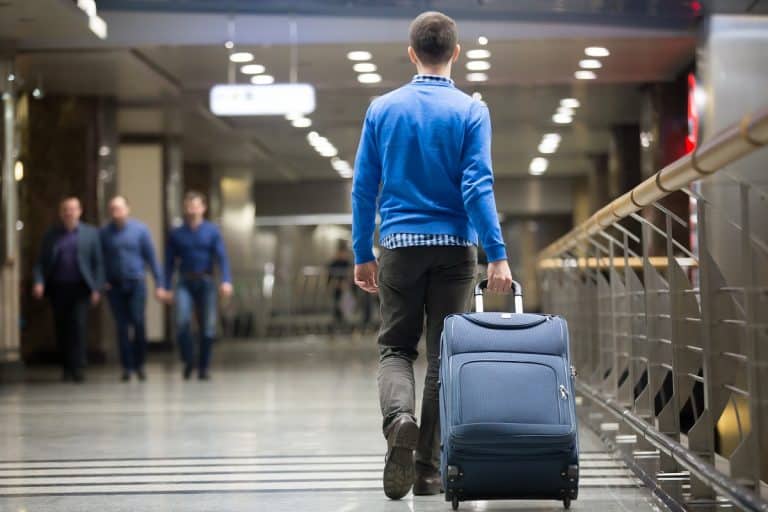 Young man pulling suitcase in modern airport terminal, Is International Carry On Smaller Than Domestic