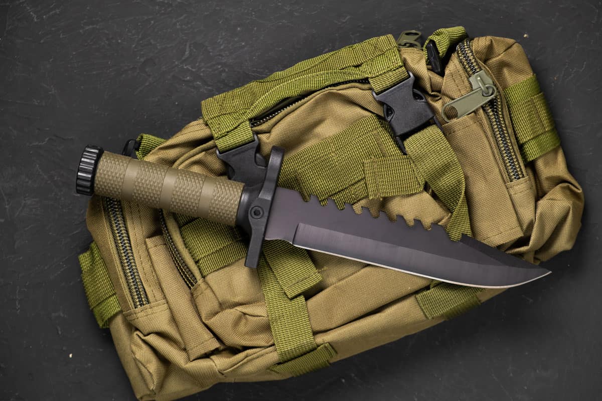 a very dangerous sharp knife on top of a green military bag and a black background