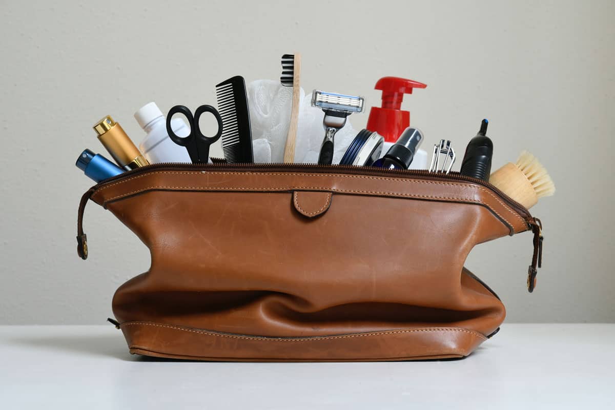 close up photo of a brown leather toiletry bag, inside are lipstick, scissors, razor, comb, pullers, brush, lotion, shampoo