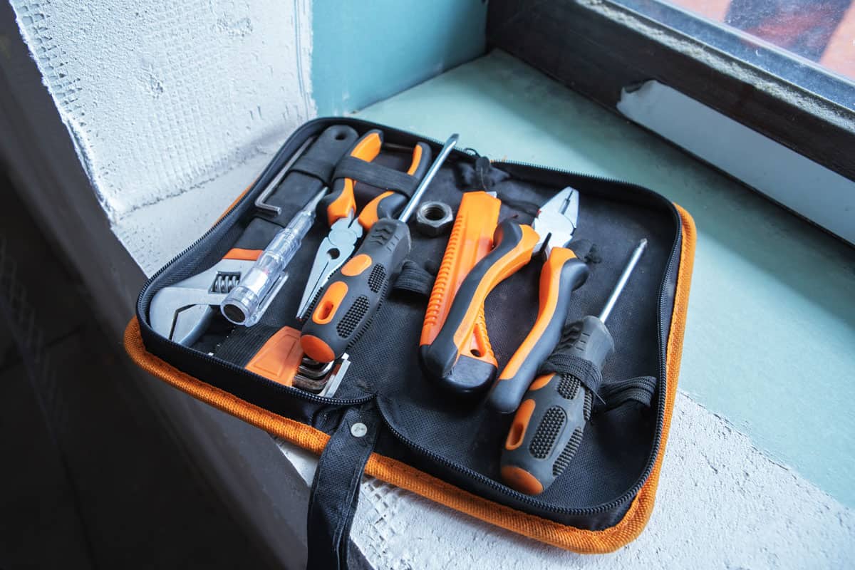 different types of small tools inside an orange tool case beside the window