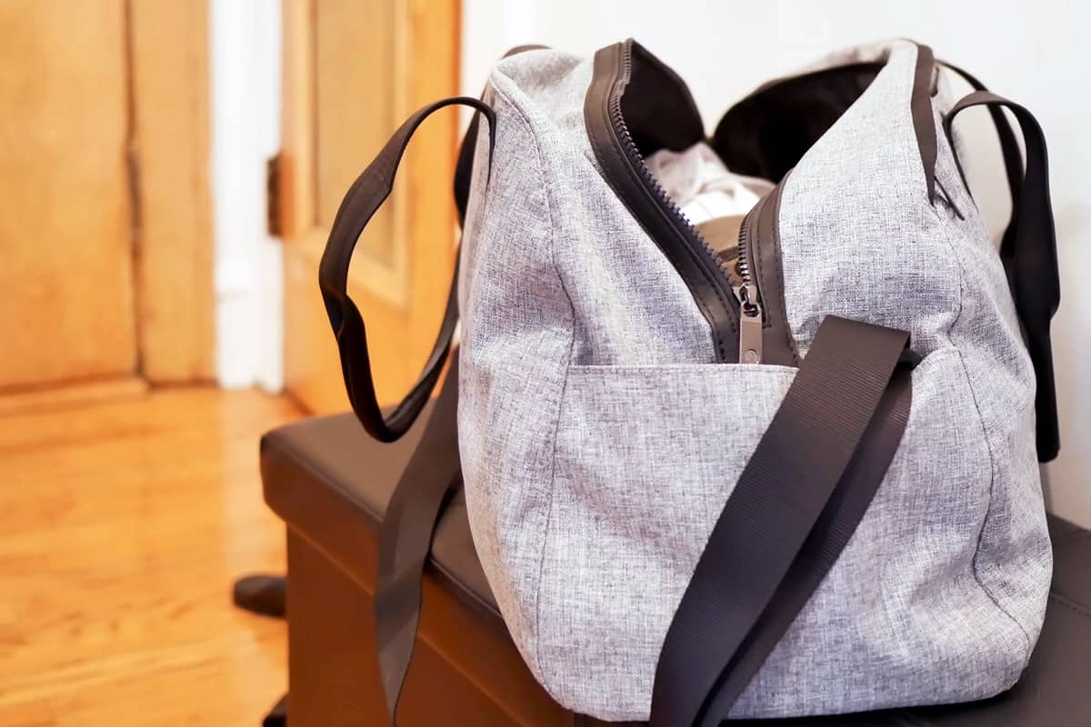 grey duffel gym bag for sport and fitness, an unbranded open bag full of clothes on the table with room background and copy space.
