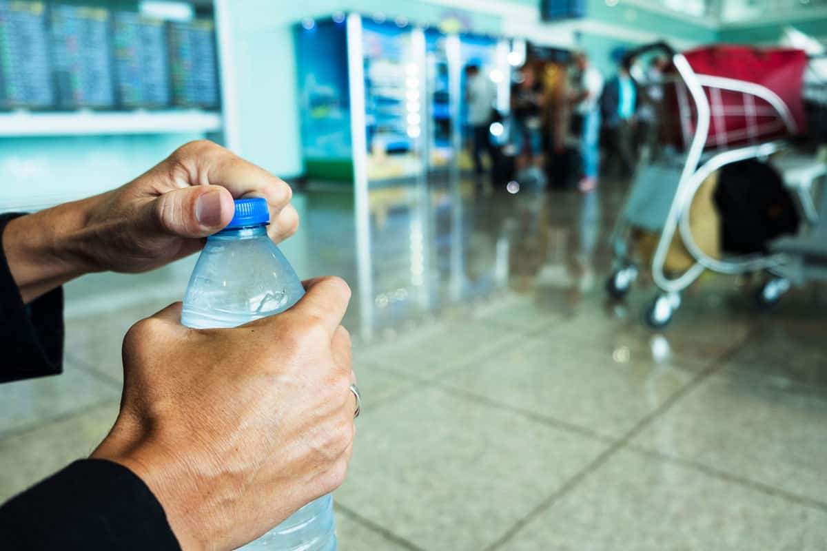 man with black sleeve, opening a plastic bottle of water on the airport terminal