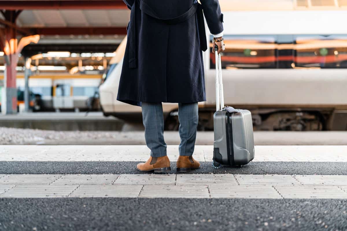 photo of a man holding rolling luggage waiting for a bus to ride home