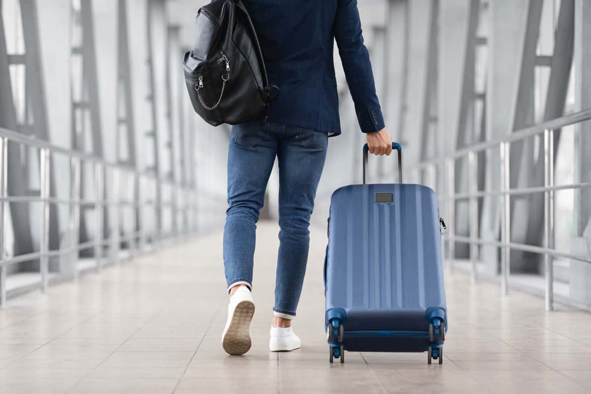 photo of a man pulling dark blue spinner luggage to the airport terminal for flight