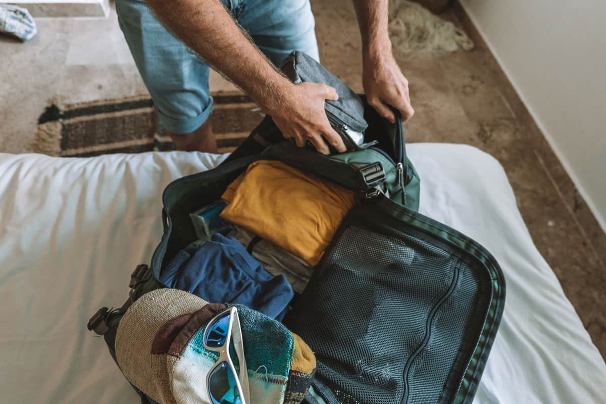 photo of a man wearing shorts, packing clothes and personal stuffs on the luggage on the bed room