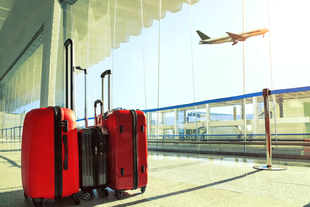 photo of a two red luggage and one grey luggage on the middle on the airport terminal