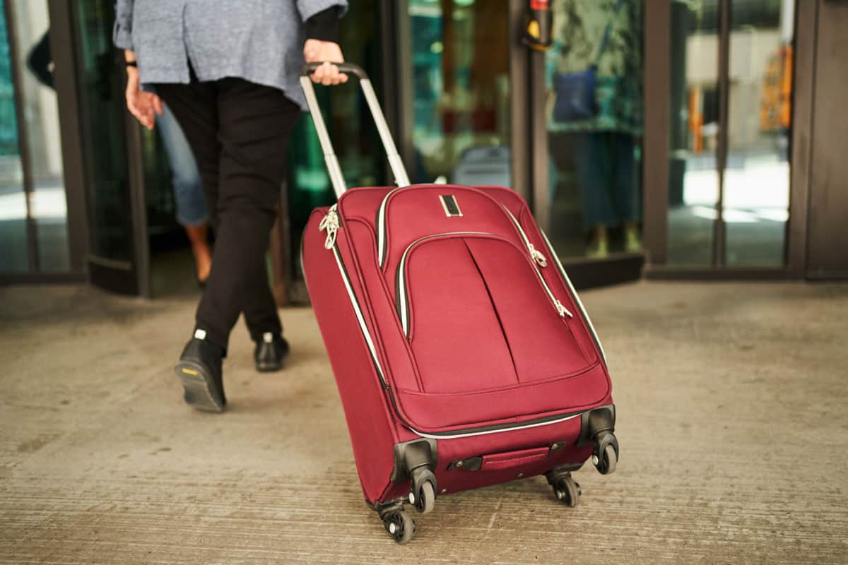 photo of a woman pulling spinner luggage, red colored luggage to the hotel