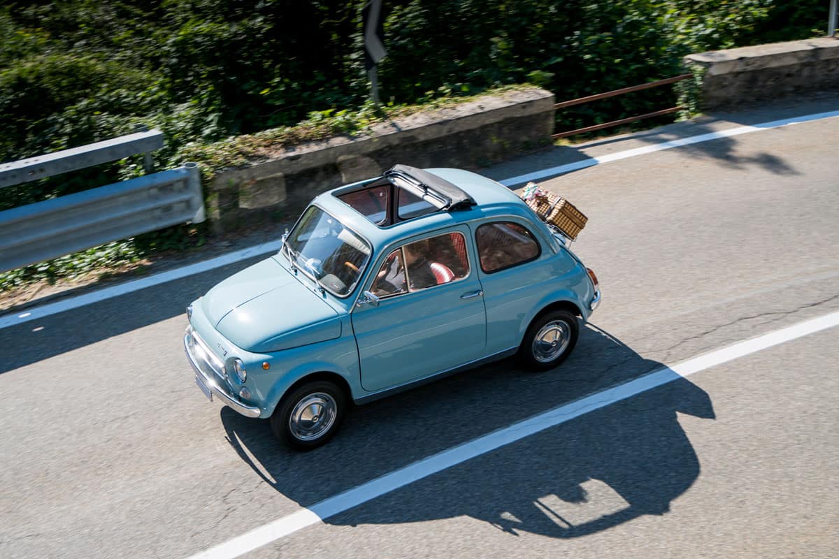 vintage sky blue painted fiat 500 car captured along side of the road with open roof