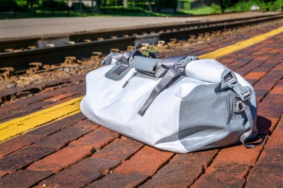 waterproof duffel beyond the yellow line at a train station platform - travel concept