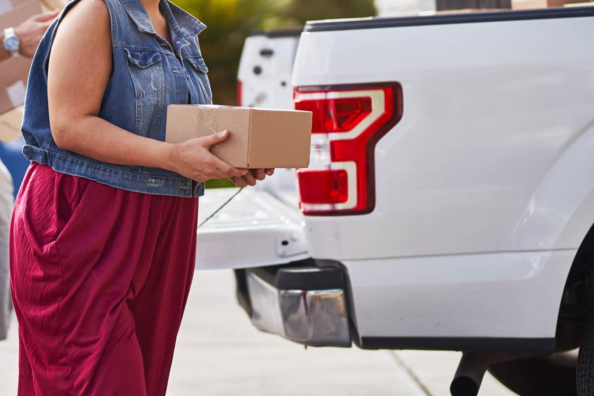 woman unloading a box of package on the white pick up truck bed