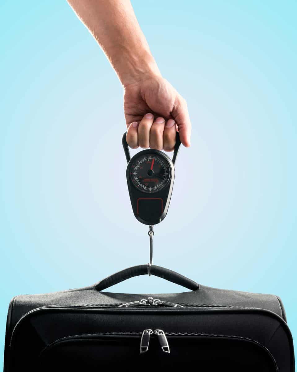 Hand weighing black suitcase on blue background
