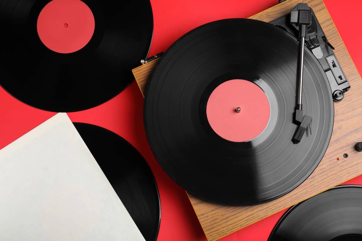Modern player and vinyl records on red background, flat lay

