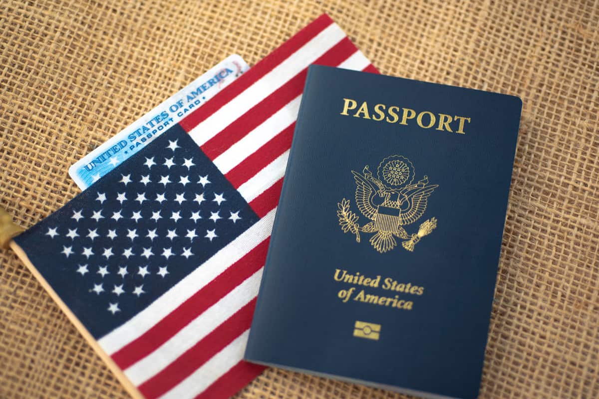 Passport card of USA covered by American Flag next to US international passport on burlap surface.