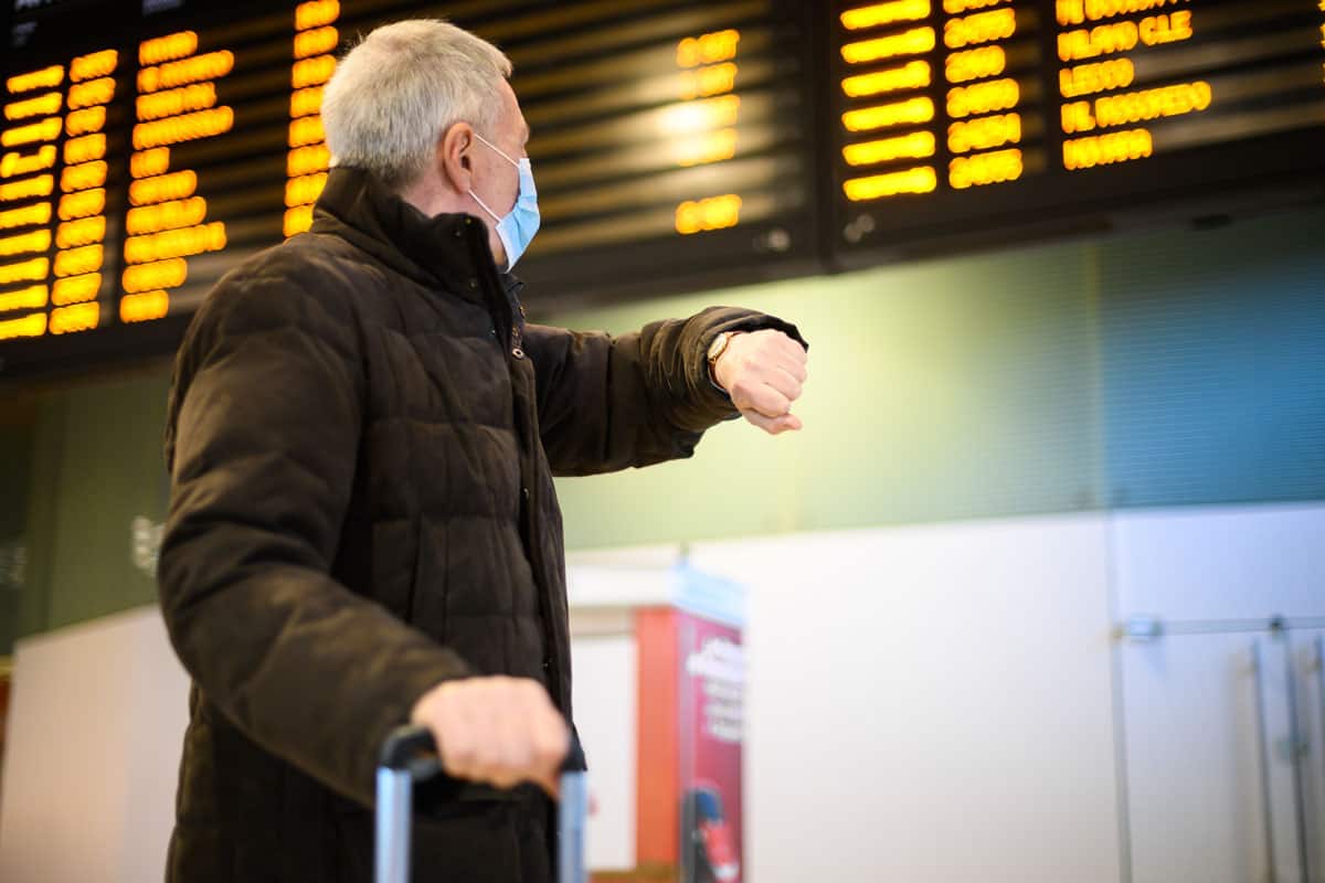 Senior man wearing a protective mask against Covid 19 in a train station checking the time