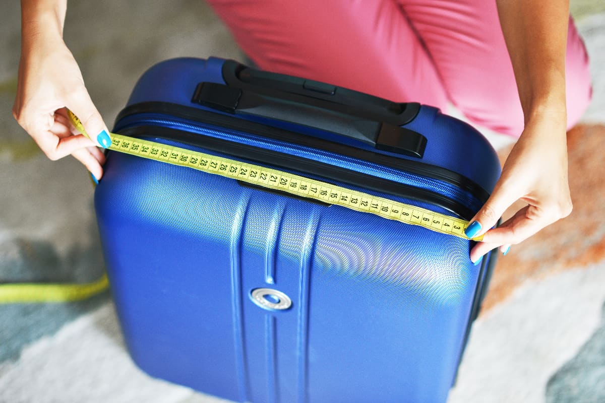 Young woman measuring travel luggage or suitcase before flight