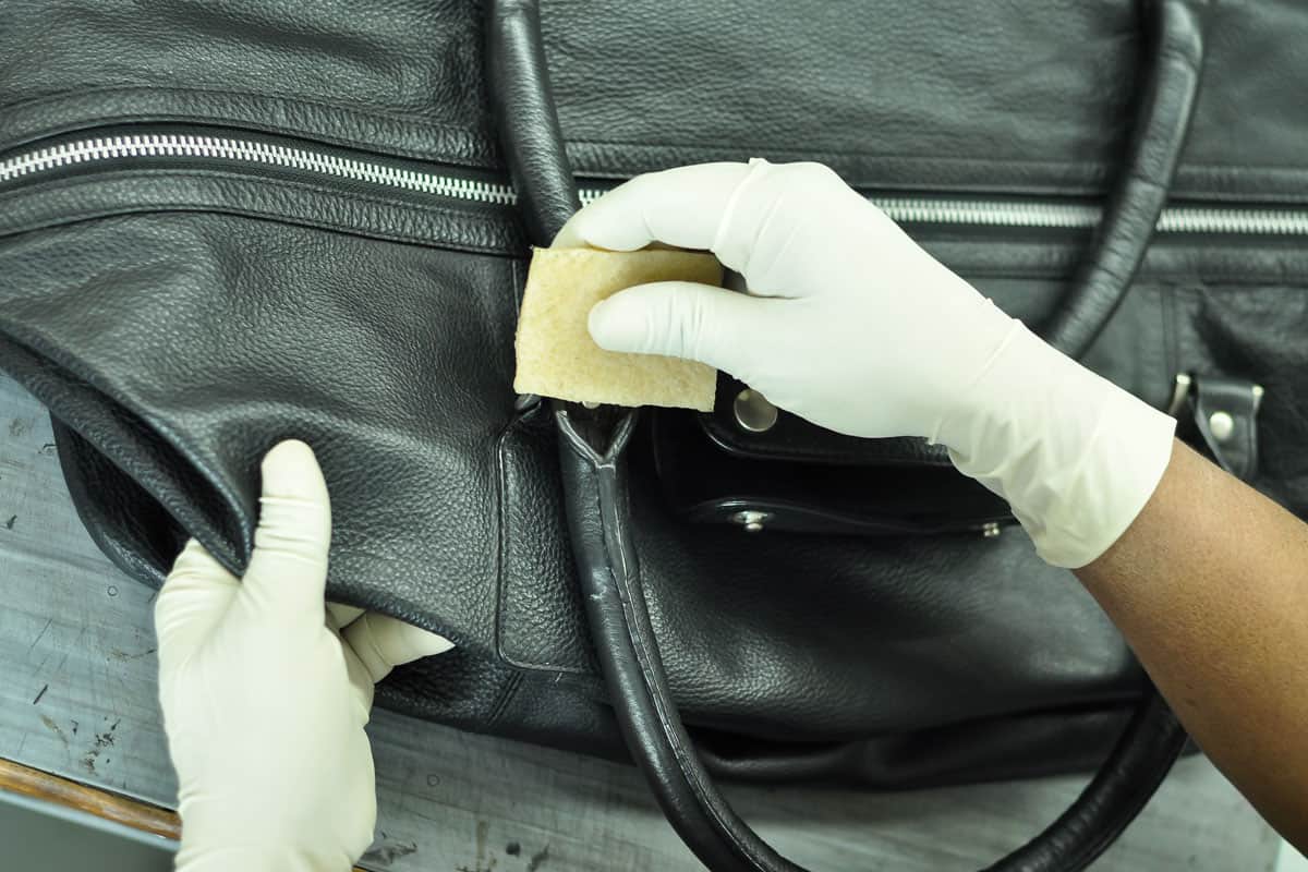 photo of a man wearing white safety rubber gloves hand cleaning the beis weekender bag