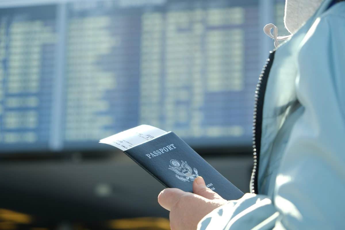 A woman with a US passport and boarding pass in the hands of the airport departure board
