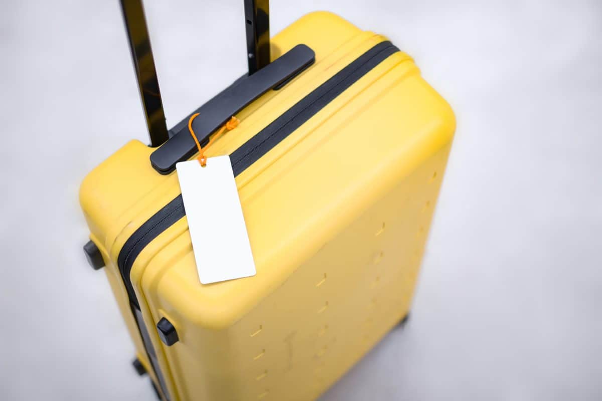 Close up mock up brand tag or name tag tied to yellow thick suitcase, concept of product logo design template on travelling tourism, travel through destination in airport, with blur bright background
