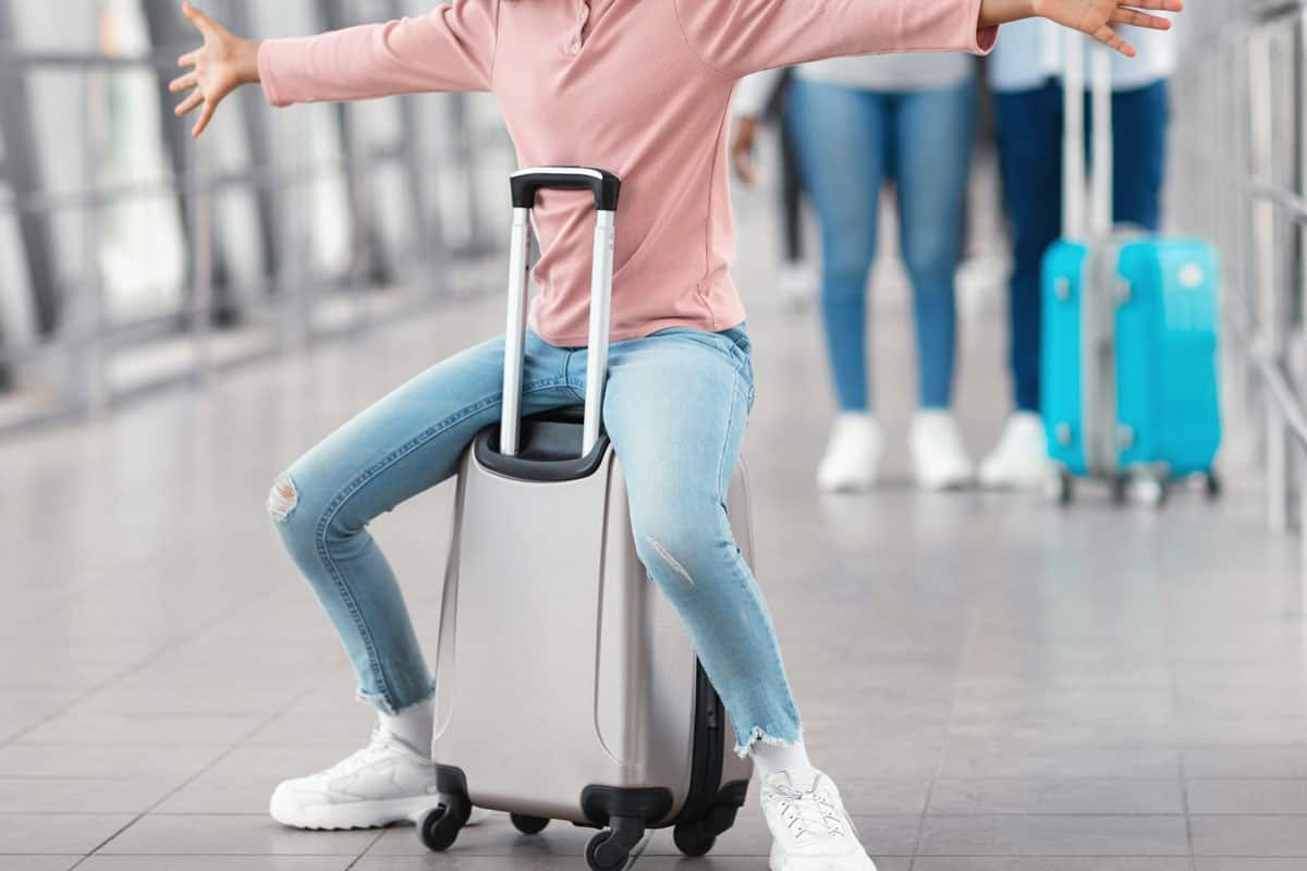 Joyful excited black girl sitting on bag and having fun in airport
