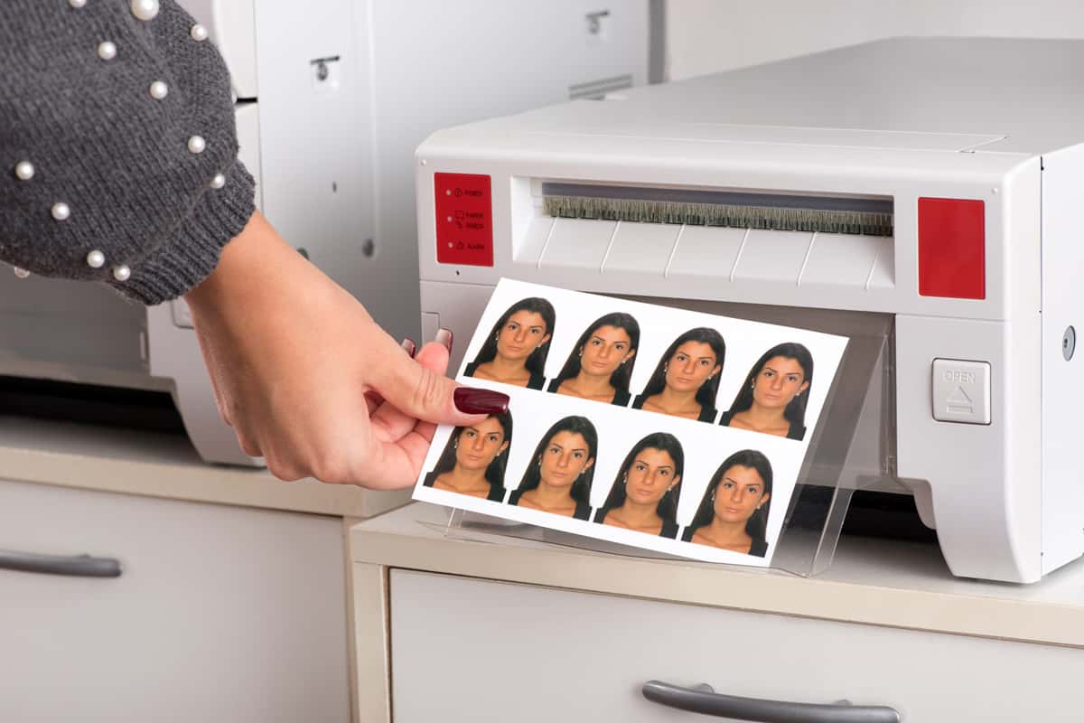 Set of just printed passport photos of a young woman exiting the printer with the hand of a woman reaching for the sheet in a close up view.
