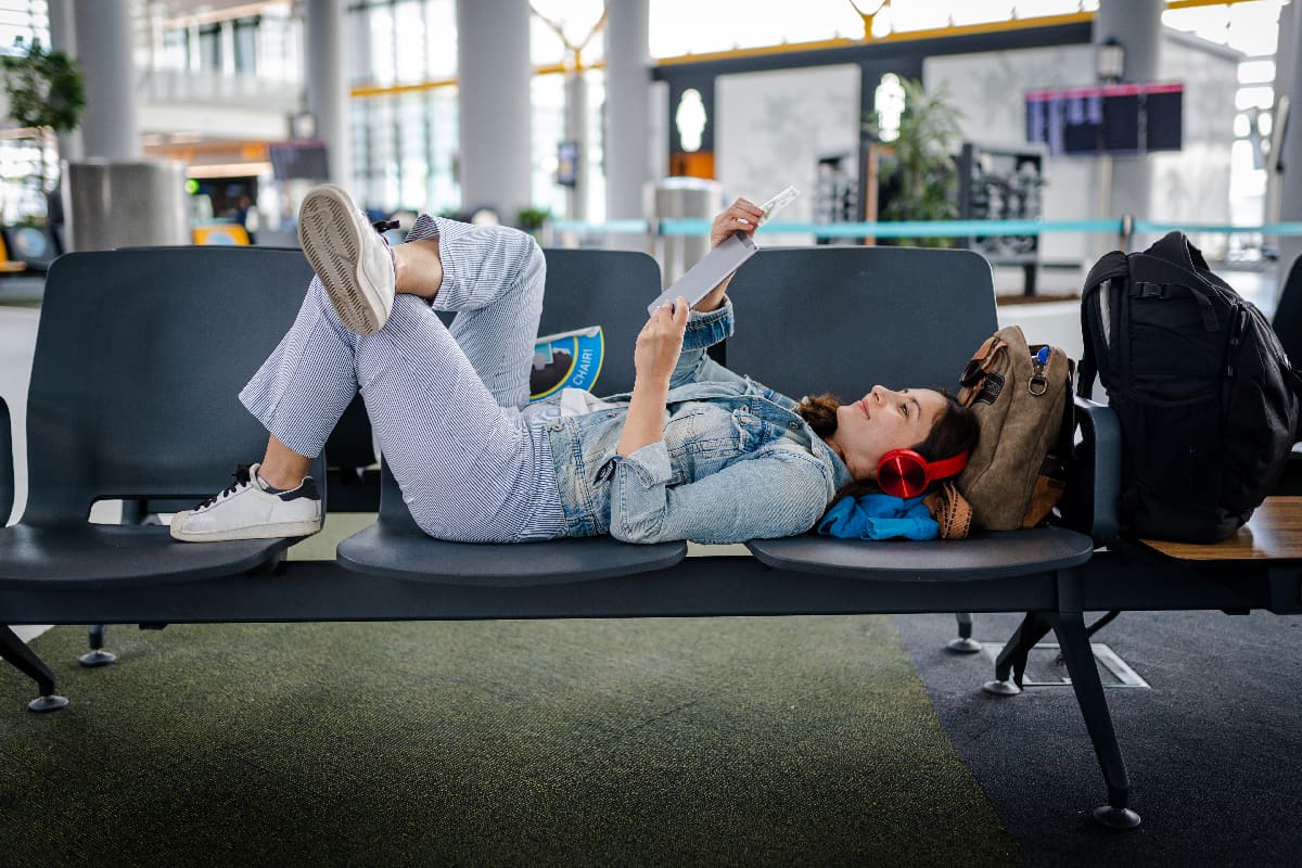 Woman waiting for delayed flight and reading digital book on chairs
