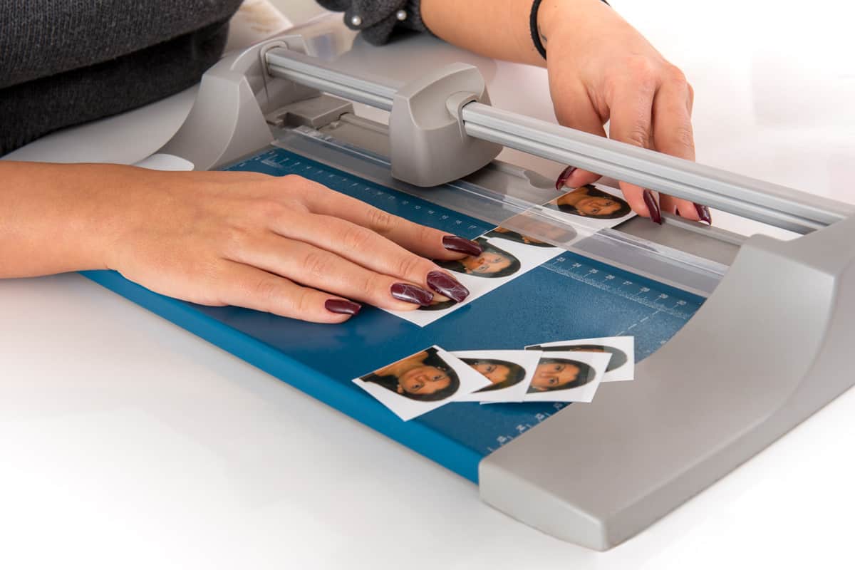 Woman cutting and sizing passport photos in a photographic studio on a small portable guillotine in a close up view of her hands.